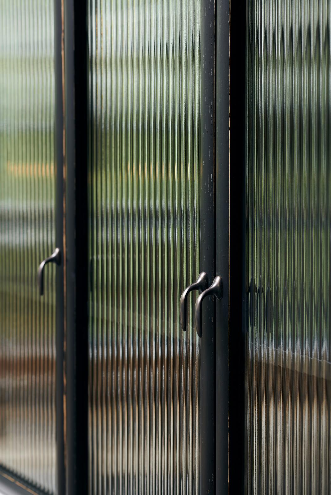 A close and oblique view of a bobbin black Haberdasher’s wall cupboard with reeded glass and oxidised brass pull hooks.
