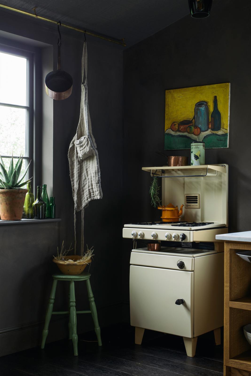 A quiet corner of a warm and inviting Haberdasher’s kitchen features a long sink run with a Carrara marble worktop. Adorned with a luscious green potted plant, vintage items, an orange teapot, a still art painting, and a beloved white gas stove, this kitchen creates a lovely exhibitionist space that is both beautiful and practical.