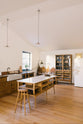 An oblique view of a warm and spacious Haberdasher’s kitchen features a sink run with a copper worktop, an Arabescato fluted sink, a small prep table with a Carrara marble countertop, and a freestanding pantry with glazed doors. Adorned with vintage furniture and items, artisan ceramics, pleat porcelain lights, large wooden tapas boards, and a delicate bird bunting in the corner of the window, this kitchen creates a contemporary yet nostalgic space.