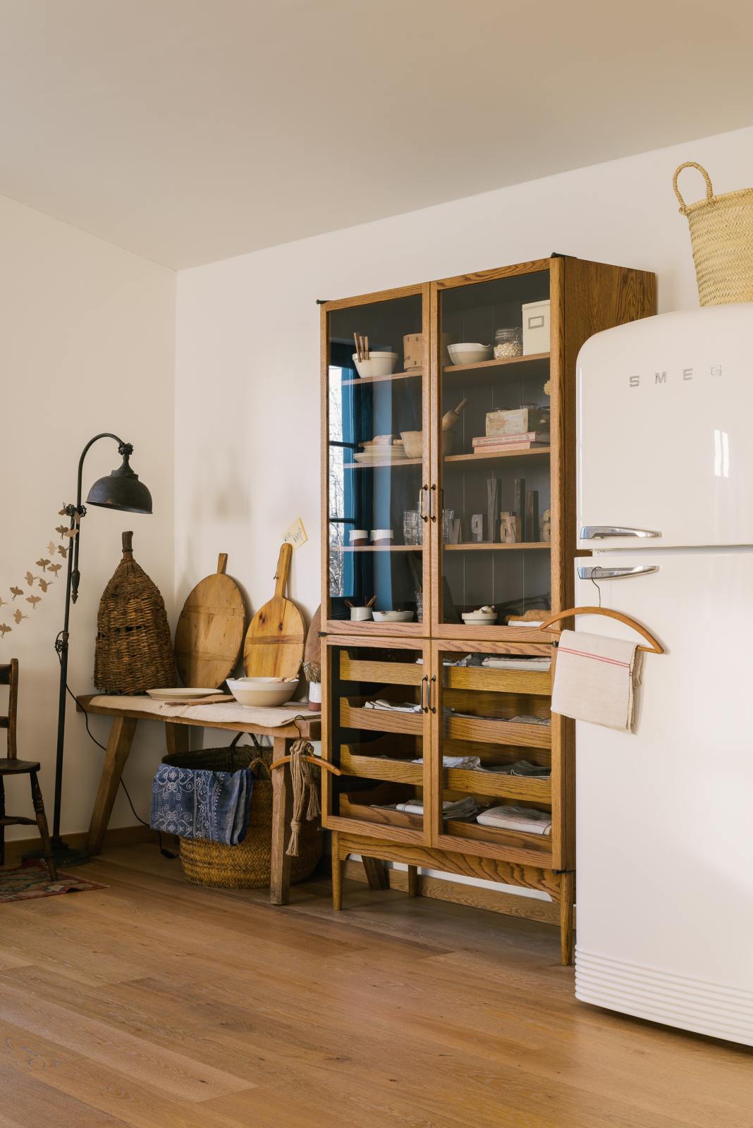 A closer look at a warm and spacious Haberdasher’s kitchen featuring a freestanding pantry with glazed doors. Adorned with vintage furniture and items, artisan ceramics, wicker baskets, tea towels, large wooden tapas boards, and wooden letterpress, this kitchen creates a contemporary yet nostalgic space.
