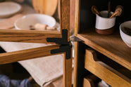 A closer look at a warm and spacious Haberdasher’s kitchen features a freestanding pantry with glazed doors. Adorned with vintage items, artisan ceramics, tea towels, and oxidised brass hinges, this kitchen creates a contemporary yet nostalgic space.