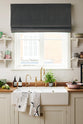 A closer look at a vibrant Shaker kitchen’s sink run with a solid oak worktop, a single Belfast sink, an aged brass Ionian tap, and Shaker shelves. Lovingly decorated with beautiful ceramics and drinking glasses, luscious green vegetables, and illustrative tea towels, it creates a characterful and inviting space.