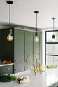 A close-up of the central island in a bright, sophisticated Bakehouse Green shaker kitchen, featuring a double Belfast sink with an aged brass Ionian tap and Silestone worktop, styled with Scandinavian furniture and a calming green palette.