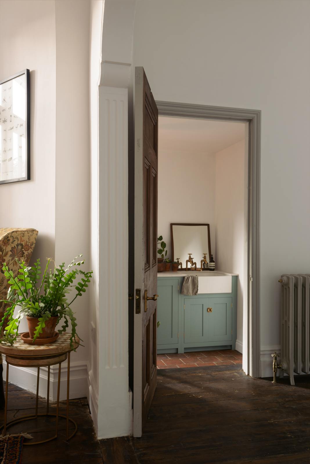 A top angled view of a beautifully detailed alcove features a Trinity Blue shaker kitchen with an L-shaped cooker and sink run. The kitchen includes a countertop cupboard topped with Carrara marble and a freestanding prep table in linen white with a copper worktop. The setting is in a well-preserved house with its original floorboards.