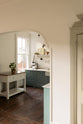 An open door in a well-preserved house with original floorboards reveals a small Trinity Blue scullery room, featuring a Carrara marble countertop, a single Belfast sink with aged brass Mayan taps, and warm terracotta tiles.