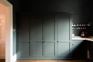 A charcoal-black, classic shaker kitchen features a U-shaped sink and cooker run with Carrara marble worktop and a bank of fitted pantry cabinets. Beautifully decorated with a colourful collection of mugs, a striking red mixer, and a silver toaster machine, the family kitchen strikes a wonderful balance between modern style and timeless character.