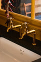 A close-up of a single fluted Belfast sink and aged brass Mayan taps of a busy and vibrant Refectory Red Shaker kitchen.