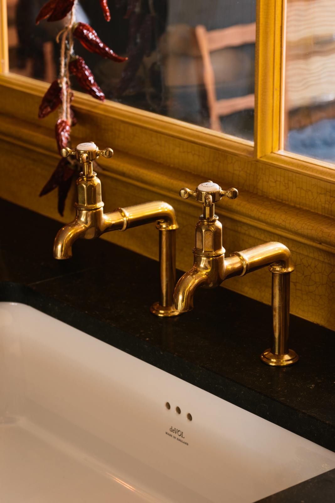 A close-up of a single fluted Belfast sink and aged brass Mayan taps of a busy and vibrant Refectory Red Shaker kitchen.