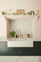 A close-up view of the Bakehouse Green shaker kitchen features a double Belfast sink, an aged brass Ionian tap, and a Carrara marble splashback set within the concave of the chimney.