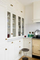 A closer look at the small but functional white linen kitchen featuring a shaker canopy, glazed cupboards, drawers, and a white porcelain splashback.