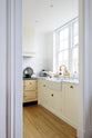 A peek inside the archway to a small but functional shaker kitchen features a white linen, complete with an L-shaped layout that includes a cooker and sink run topped with Carrara marble.