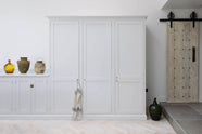 A spacious and artisan Shaker kitchen features an off-white L-shaped sink run with a Carrara marble worktop, a large pantry-blue kitchen island, and a bank of full-height cupboards. Cleverly decorated with vintage ceramics serving as artistic displays, it creates a simple yet intriguing kitchen space.