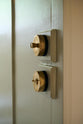 A close-up and angled view of a deVOL’s petite oval dimmer switch and petite oval toggle switch in a traditional and warm heirloom brass finish, fitted in a simple basement kitchen of a Georgian townhouse.
