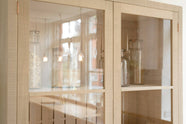 A close-up of a simple and contemporary Sebastian Cox kitchen’s glazed freestanding cupboard. Adorned with large glass containers of dried ingredients such as pasta. 