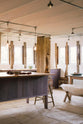 A quiet corner of a soft and spacious Sebastian Cox barn kitchen features a long sink and cooker run with a solid oak worktop, and a kitchen island with a breakfast nook. Beautifully decorated with lavender colour tints, bare pendant lights, vintage furniture, artisan ceramics, sweet potatoes, and sheep rugs, this kitchen creates an elegant and ethereal space.