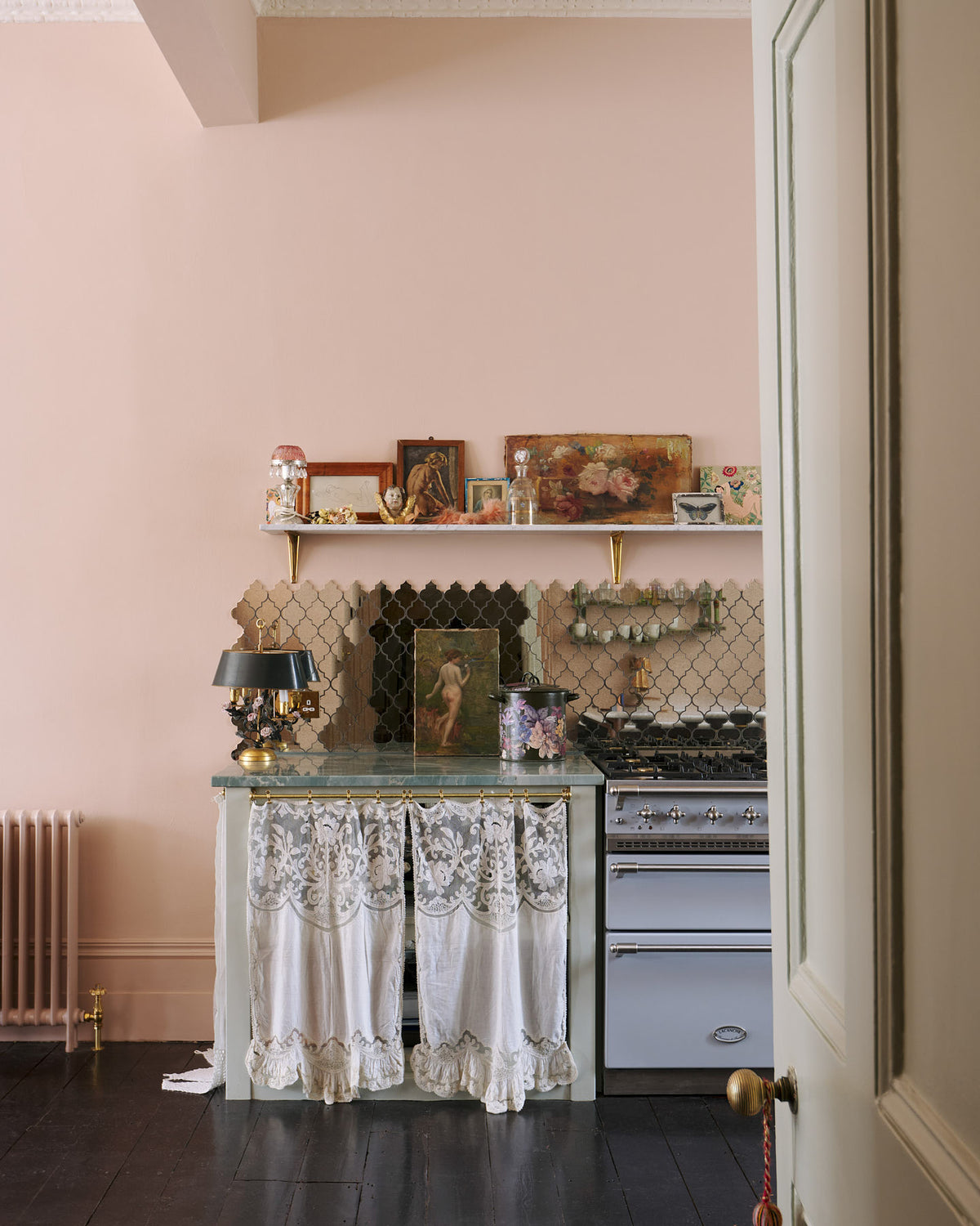 A decorative corner of a light pastel-blue classic kitchen’s cooker run with a beautiful turquoise marble worktop. The London apartment has high ceilings, worn black painted floorboards, small decorative splashback mirrors, intricate cornices, and is styled with the customer's collection of antiques.