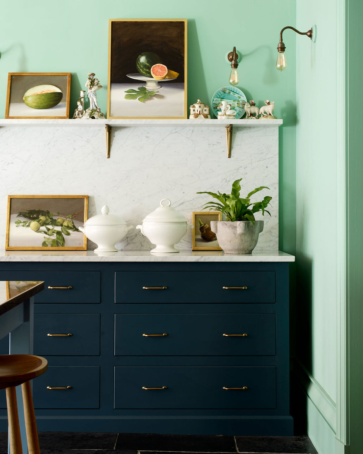 A stunning Bond Street blue kitchen features a cooker run with Arabescato marble worktop, splashback, shelf, a freestanding open larder, and one small prep table with deVOL bum stools. The room features a stunning mix of colours and character, accentuated by colourful glasses, gold-framed still life paintings and an aged brass pot filler handmade in England.