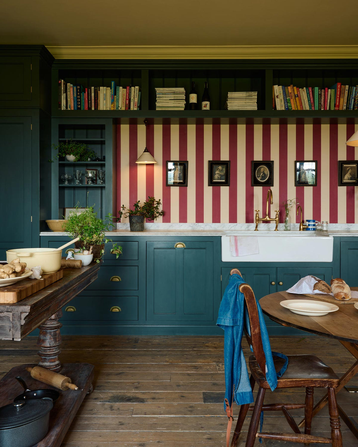 A lovely modern kitchen that retains the charm of its original structure and flooring, using the three primary colours in a muted, mature palette. The spacious kitchen features Clerkenwell Blue full-height pantry cabinet, a long sink run with a marble worktop, an open countertop cabinet, a high shelf, and a red-and-white striped splashback.