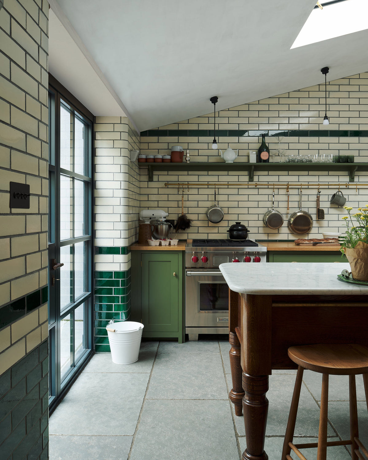 A small and quaint Wilkes green Shaker kitchen featuring a cooker and sink run with a classic oak worktop fits nicely the subway tiles splash back wall. Partnered with an Heirloom Dairy table for a touch of elegance and warmth in the otherwise busy chef's-table-experience-esque space.