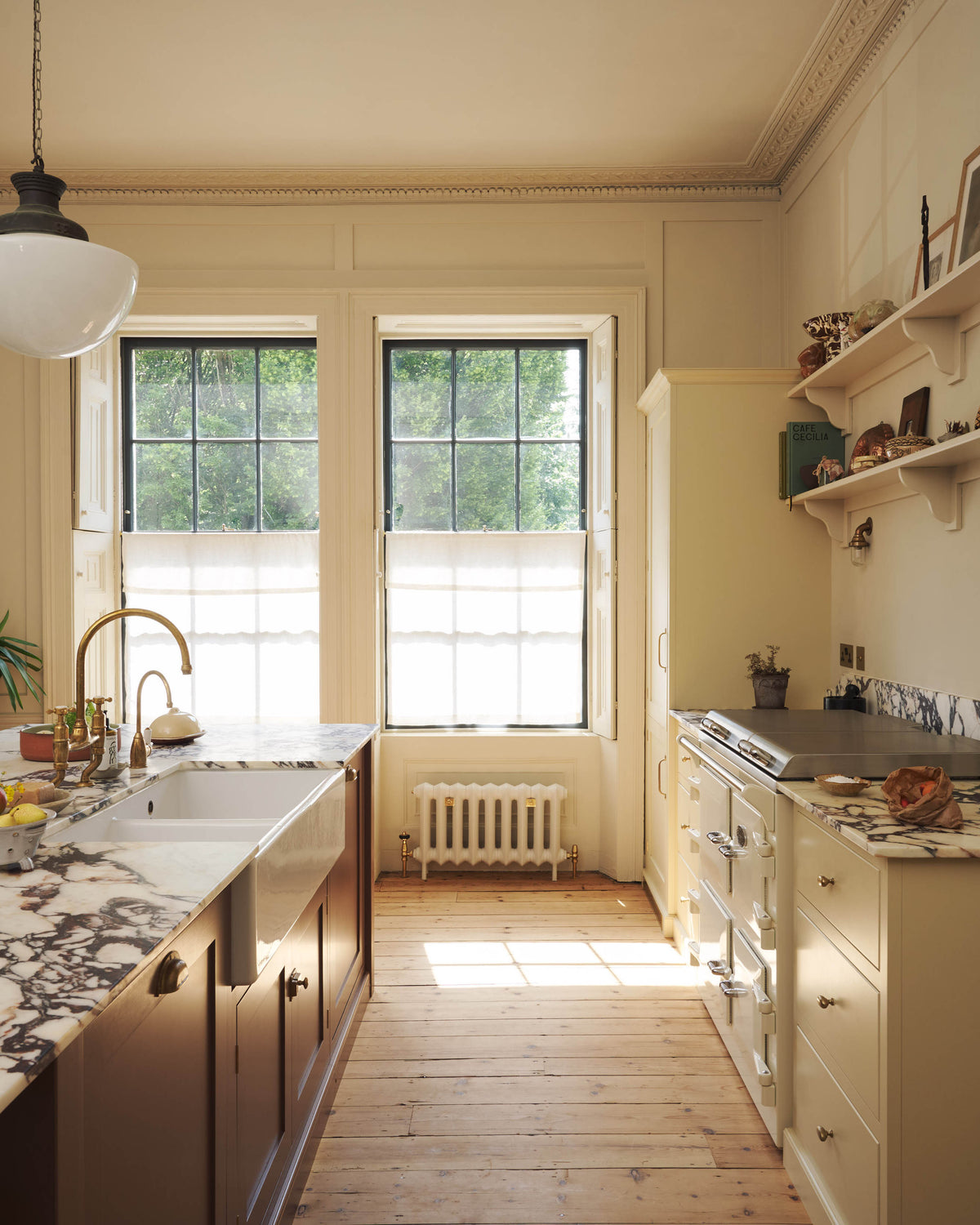 A bright, spacious, warm, and simple-yet-grand shaker kitchen featuring a large kitchen island with a Calacatta Viola worktop, a cooker run, a fridge/freezer cupboard, and long shaker shelves. Perfectly decorated with beloved vintage furniture and decor made from different natural materials, it creates a scene of absolute beauty, personality and functionality.
