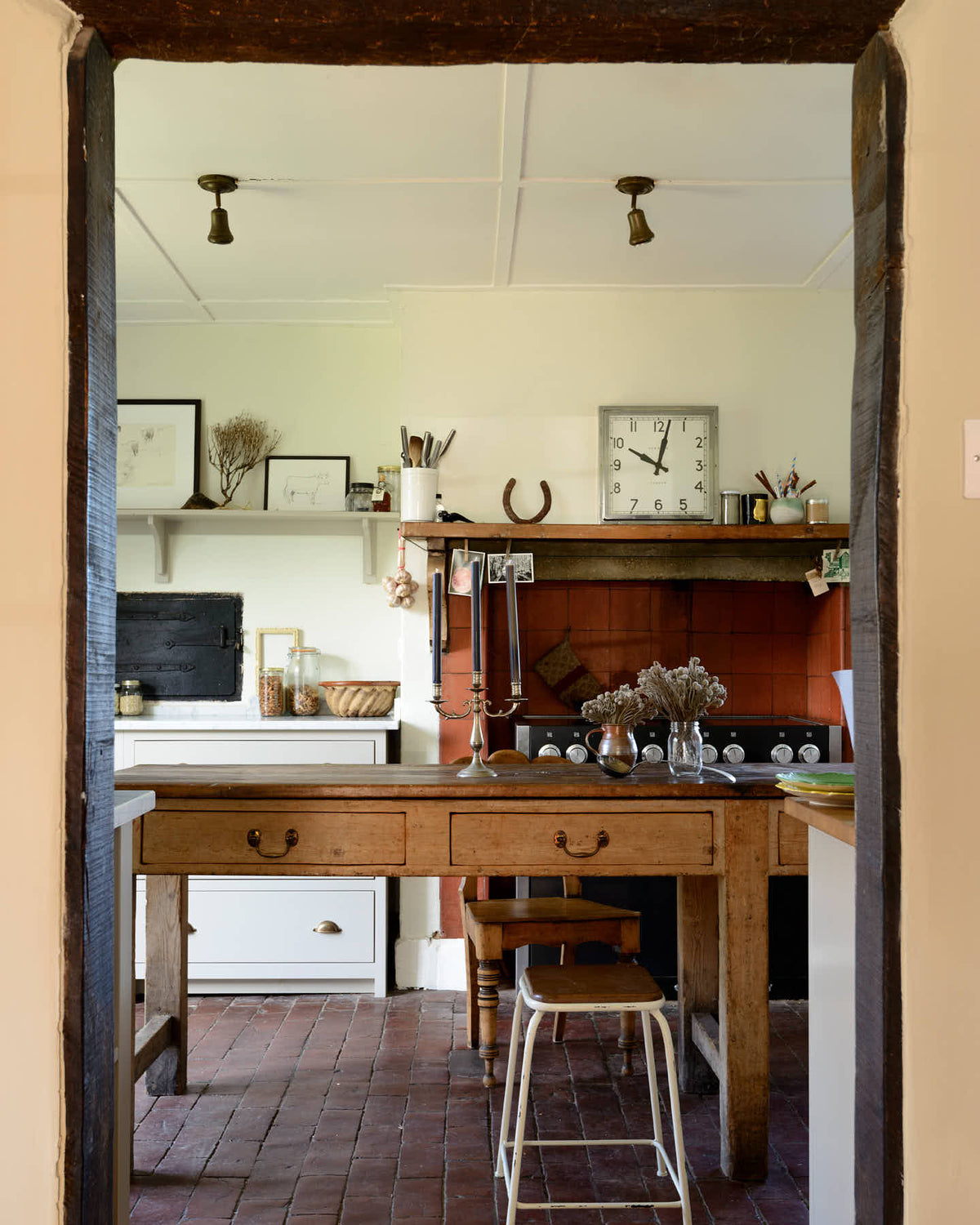 Pass the original farm’s solid oak archway is a small and quaint mushroom-coloured Shaker kitchen features a sink run made up of a mix of stave hardwood and Carrara marble worktops, a shelf, and a black stove nestled inside the original building’s chimney breast. Beautifully decorated with vintage furniture such as a large solid oak table, a silver scale, and assorted bric-a-brac, it creates a lovely social space full of character.
