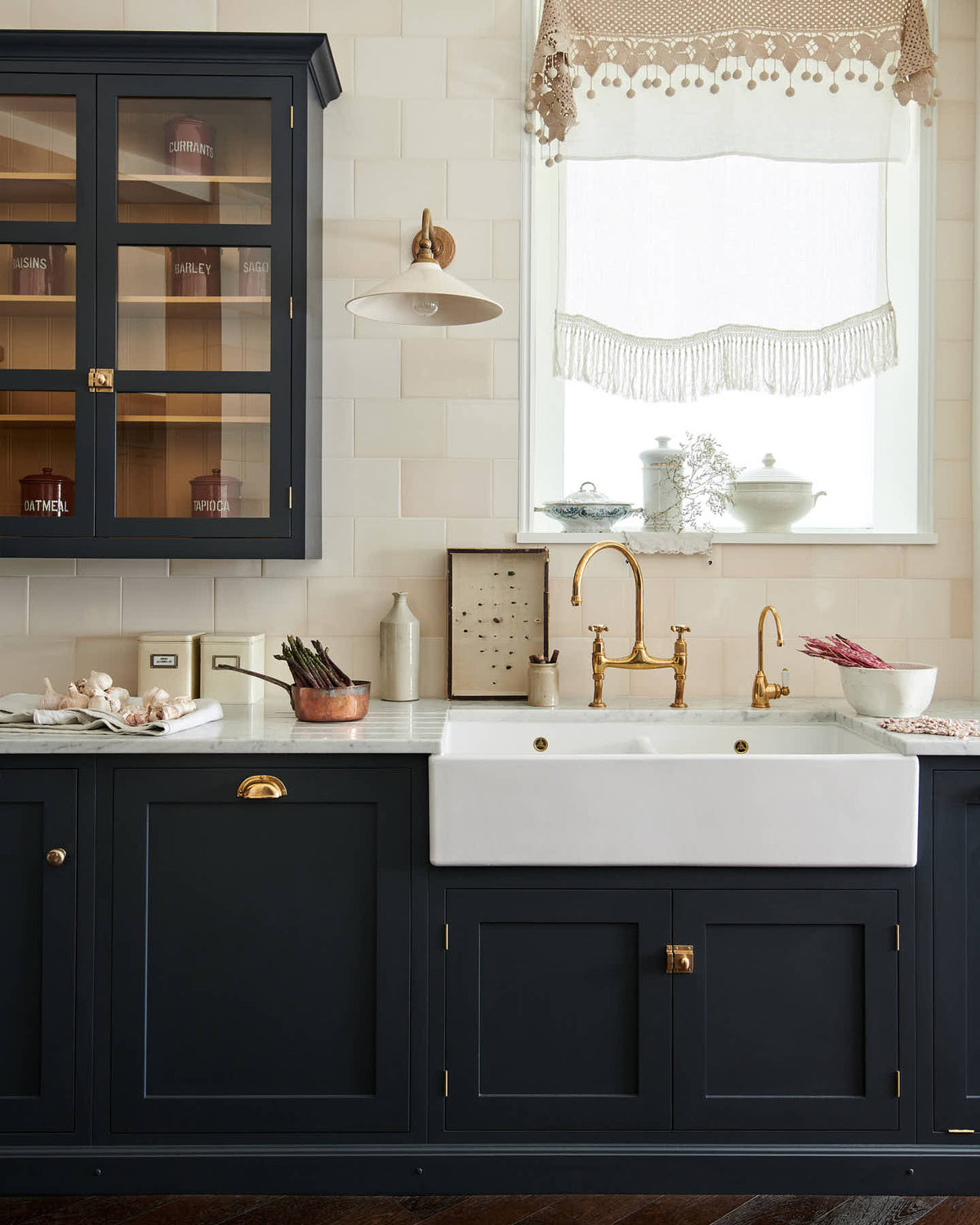 A large pantry blue shaker kitchen features a sink and cooker run with Carrara marble worktop, a double Belfast sink, an aged brass Ionian tap, wall cabinets with Scullery yellow interior, and cream subway splashback tiles. Beautifully decorated with vintage items, artisan ceramics, an antique bug display, and a deVOL Heirloom task light, the kitchen presents a thoughtfully curated mix of collected pieces that fit together effortlessly.