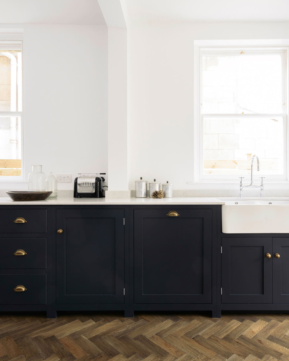 A closer look at a bright and simple pantry-blue Shaker galley kitchen features a long sink and cooker run with a double Belfast sink, an antique silver Ionian tap, silver gas cooker, and a Shaker canopy. Beautifully decorated with fundamental kitchen equipment such as a silver toaster, matching silver coffee, tea, and sugar containers, a vintage scale, and reclaimed wooden parquet, it creates a stylish and effortless space.