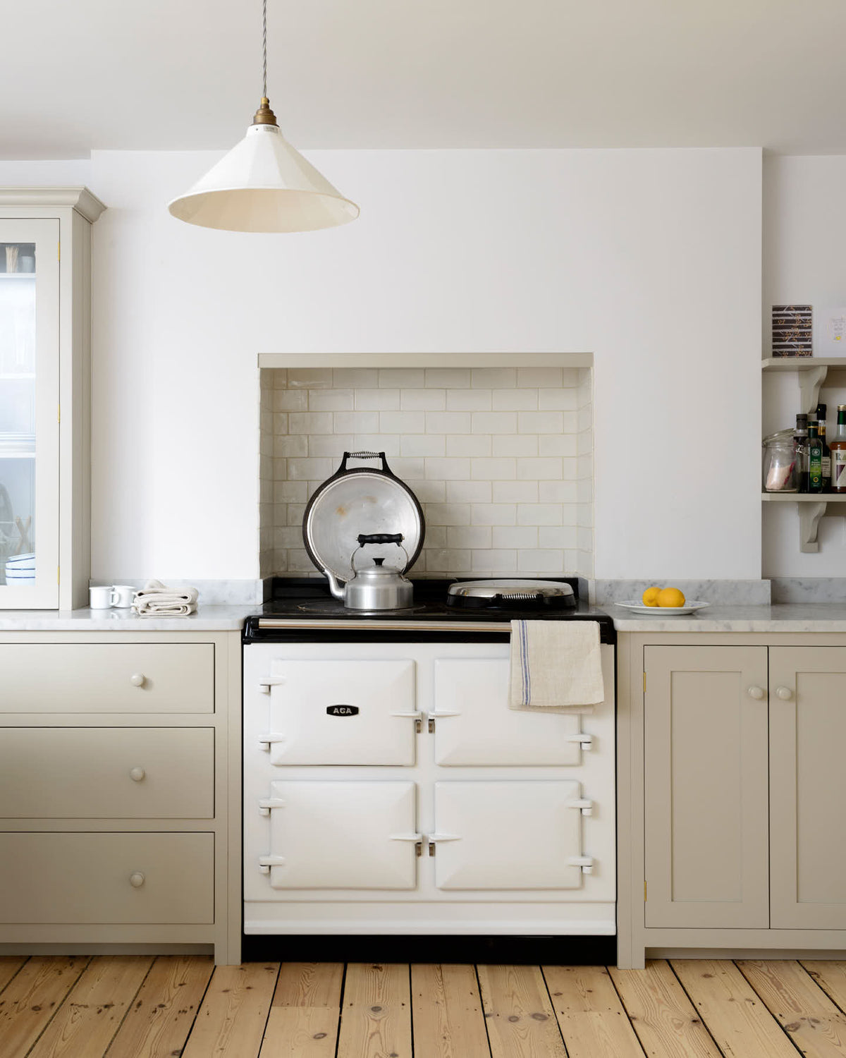 A minimalist, mushroom-coloured shaker kitchen includes a cooker around a chimney breast, a white gas stove, and a porcelain splashback.
