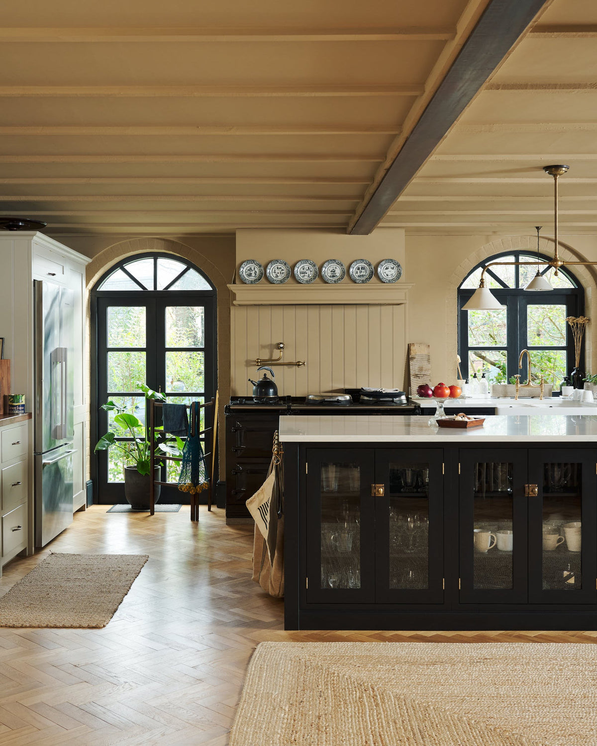Past through the glass partitions, is a wide open social space that includes a Painter's black Shaker kitchen and Mushroom pantry. Busy with a lot of kitchen utilities, plants, and beloved furniture and ceramics, the space is an incredibly inviting and comfortable family room.