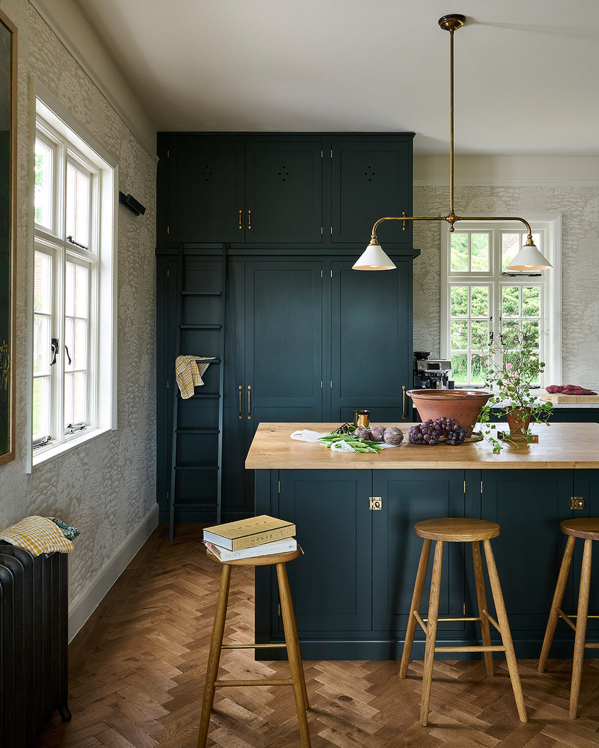 A closer look at the floor-to-ceiling pantry, which features a bespoke ladder, along with a modest kitchen island topped with solid oak that serves as a breakfast bar equipped with two iconic Helen stools.