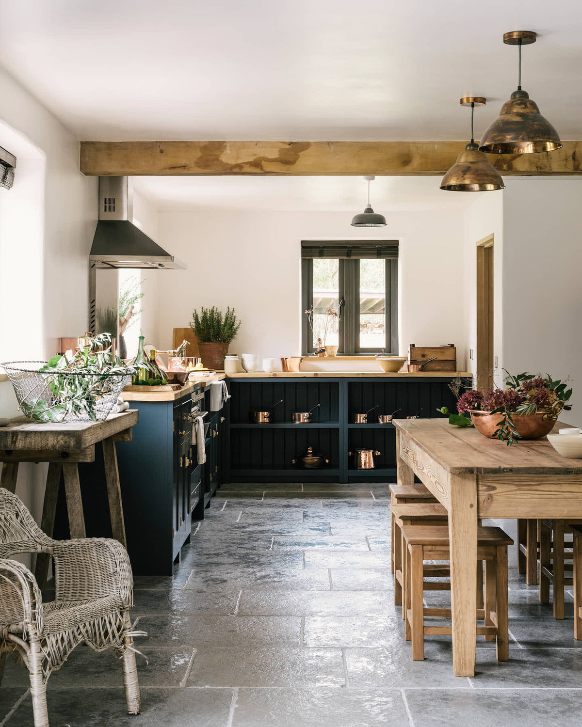 A charming cottage shaker kitchen in Pantry Blue features a cooker run, open base cabinets, and a solid oak worktop that complements the wooden ceiling beams and the vintage dining table with stools.