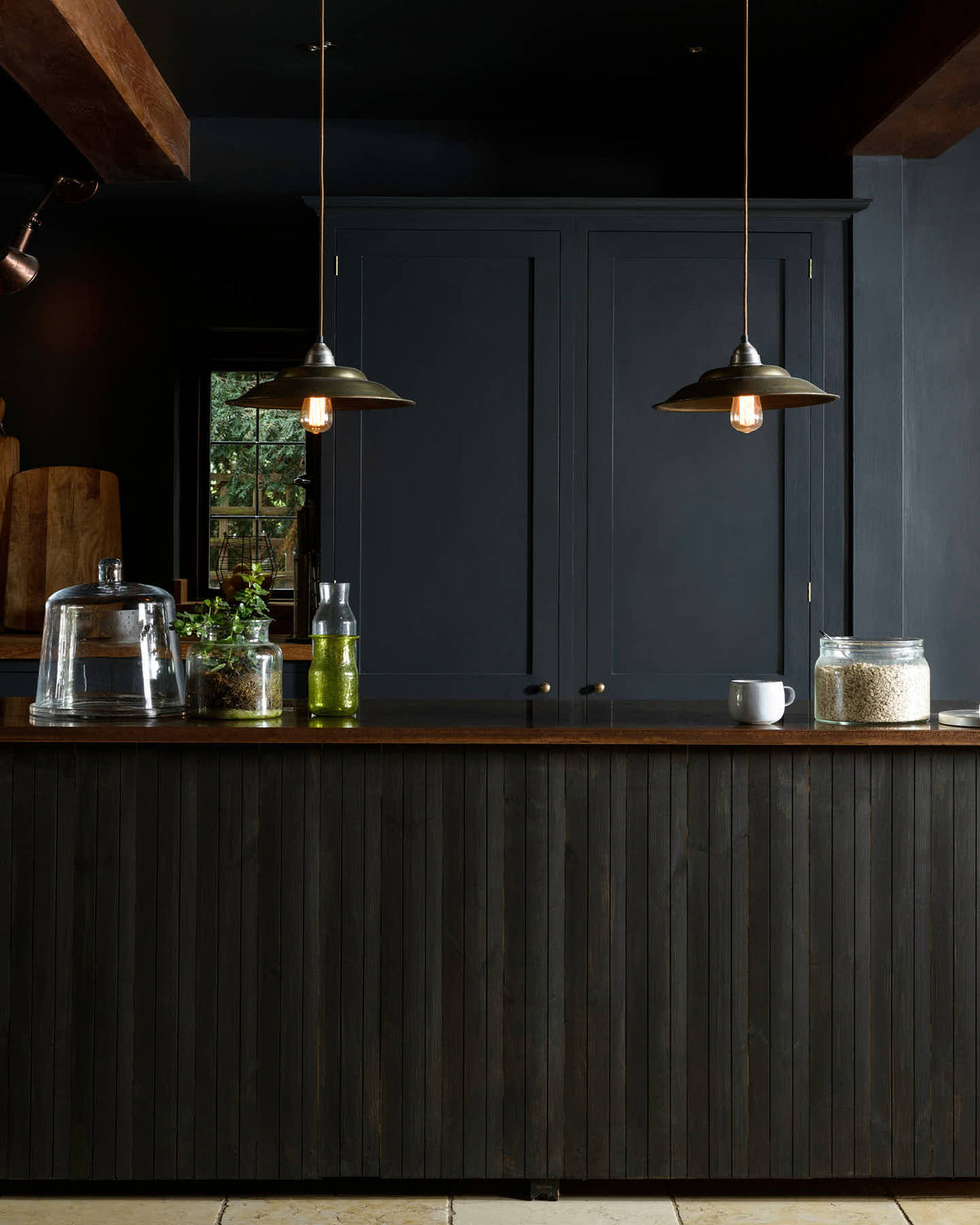 A closer look at the Pantry Blue, vintage kitchen island topped with Iroko wood. Light stone flooring enhances the space, featuring wooden ceiling accents, a large cooker splash back, and two hanging lights above the island.