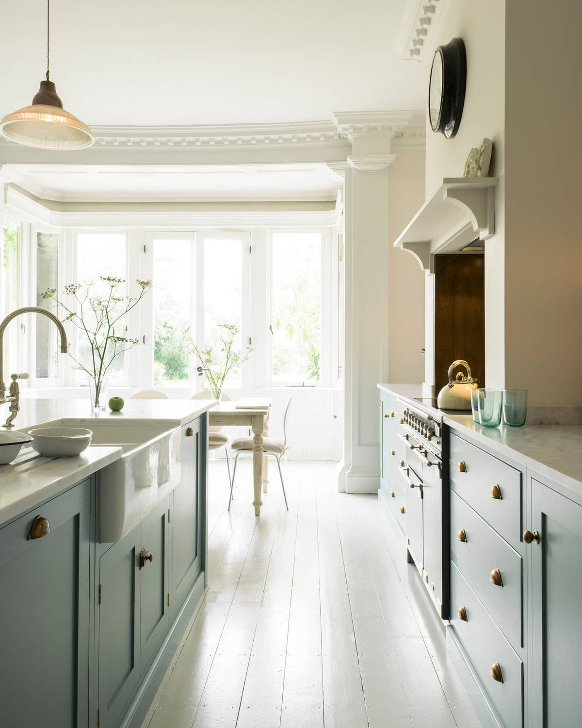 The bright pathway between the cooker and the kitchen island features a double Belfast sink, all part of the Trinity Blue shaker kitchen. In front of this area is a small conservatory with its original French doors, which let in plenty of natural light that fills the pale wooden breakfast table and cushioned chairs.