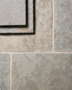 A close-up overhead view of Jaipur Brushed Limestone flooring, showing the textured surface and subtle variation in colour in each tile. Two loose tiles are stacked in the top left corner.