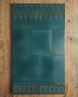 A small arrangement of handmade glossy teal wall tiles - some plain, some with decorative lace patterns - on a rustic wooden tabletop.