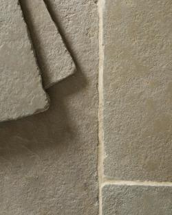 A close-up overhead view of an aged limestone floor with natural earthy tones of green, brown and grey, with two loose tiles stacked in one corner.