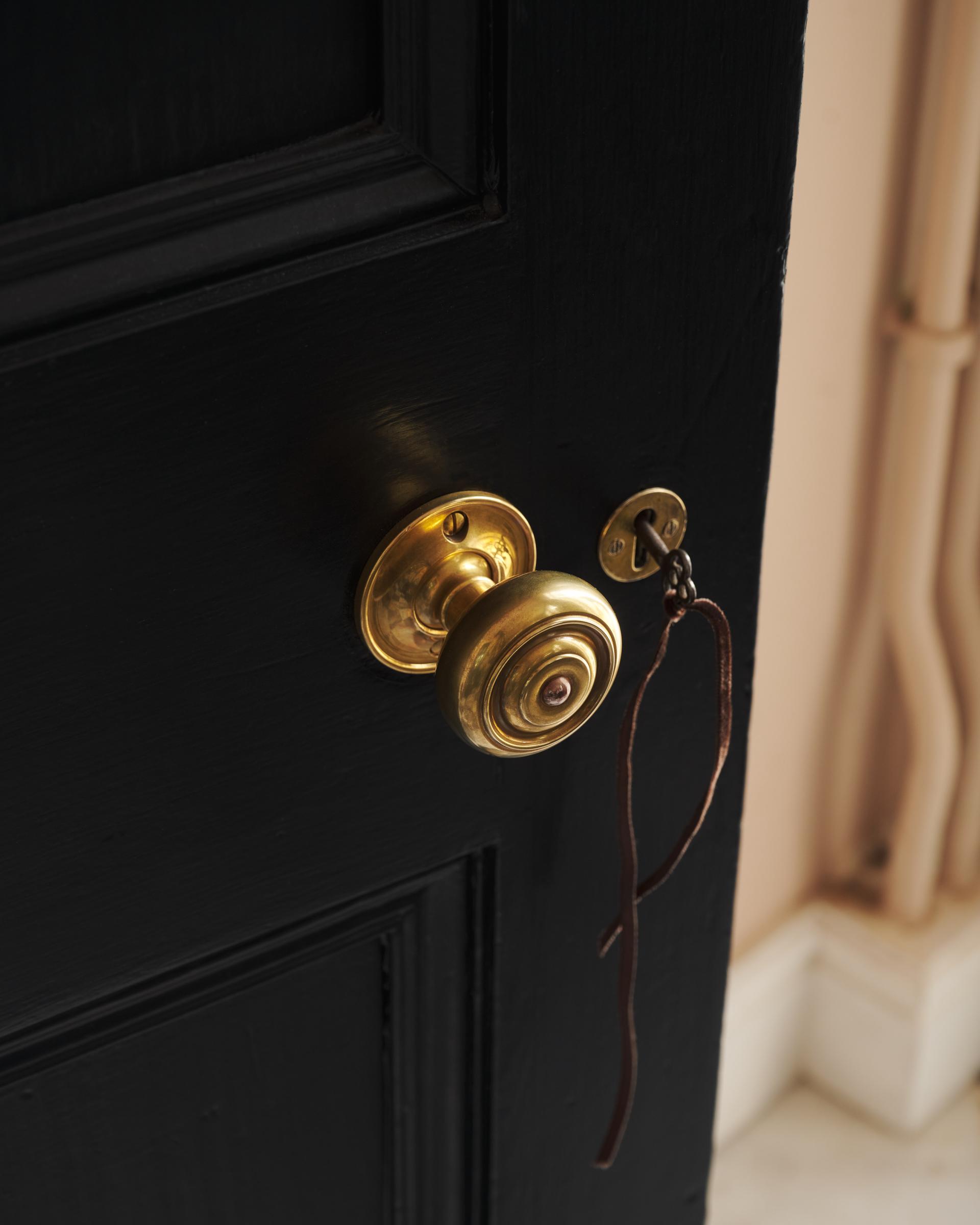 The brass knob from a side angle, leather key cord visible, with the black paintwork contrasting beautifully against a pale floor.