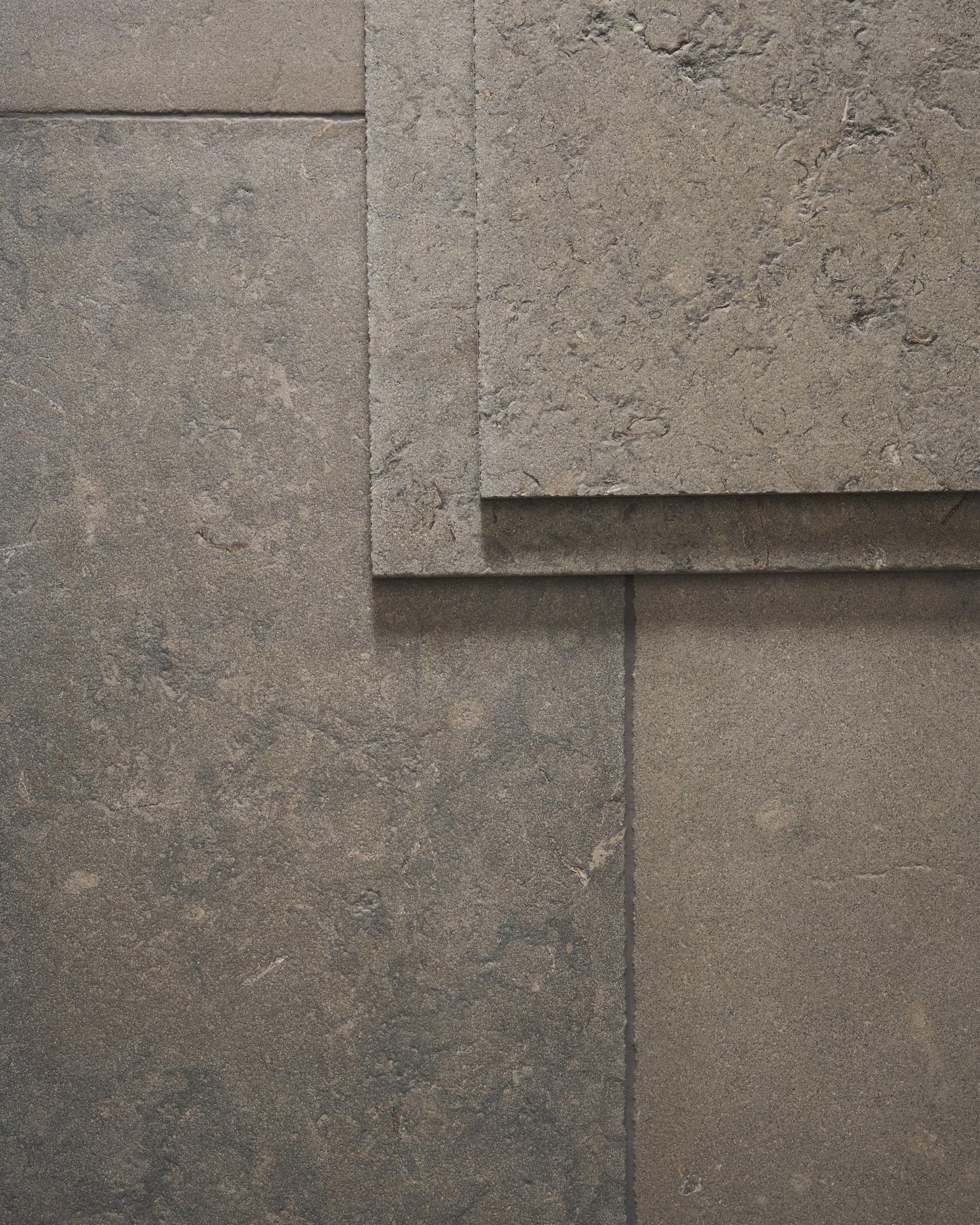 A dark grey limestone floor with a dark grout and a stack of loose tiles in the top right corner, viewed from above.
