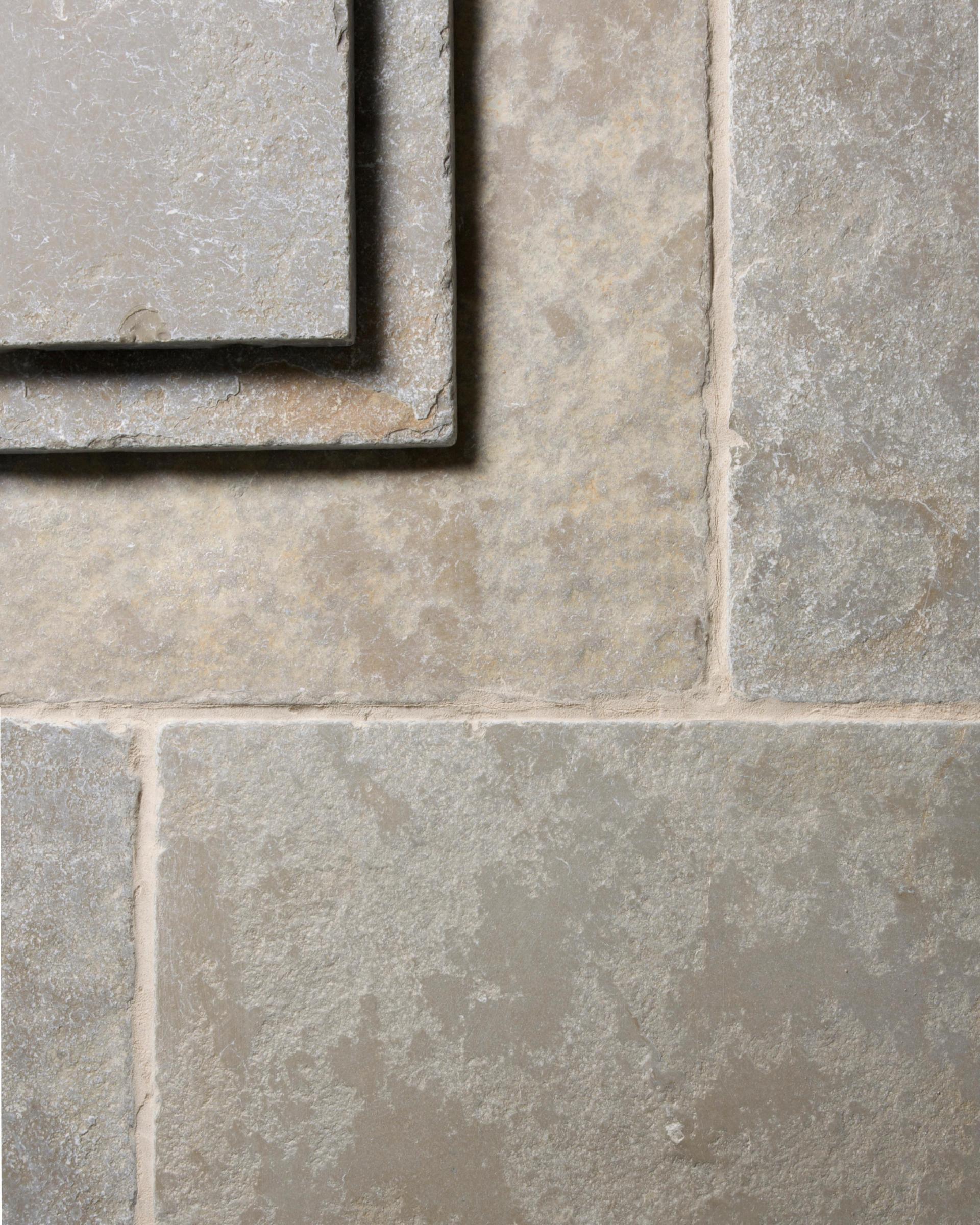 A close-up overhead view of Jaipur Brushed Limestone flooring, showing the textured surface and subtle variation in colour in each tile. Two loose tiles are stacked in the top left corner.
