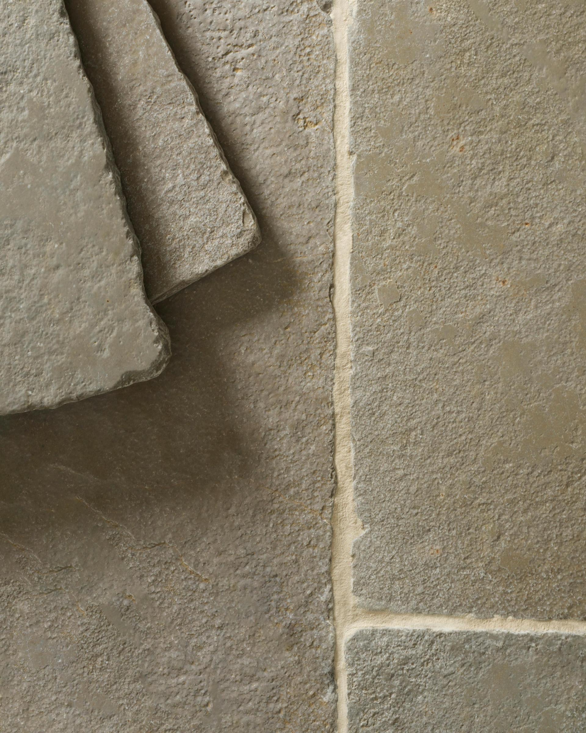 A close-up overhead view of an aged limestone floor with natural earthy tones of green, brown and grey, with two loose tiles stacked in one corner.