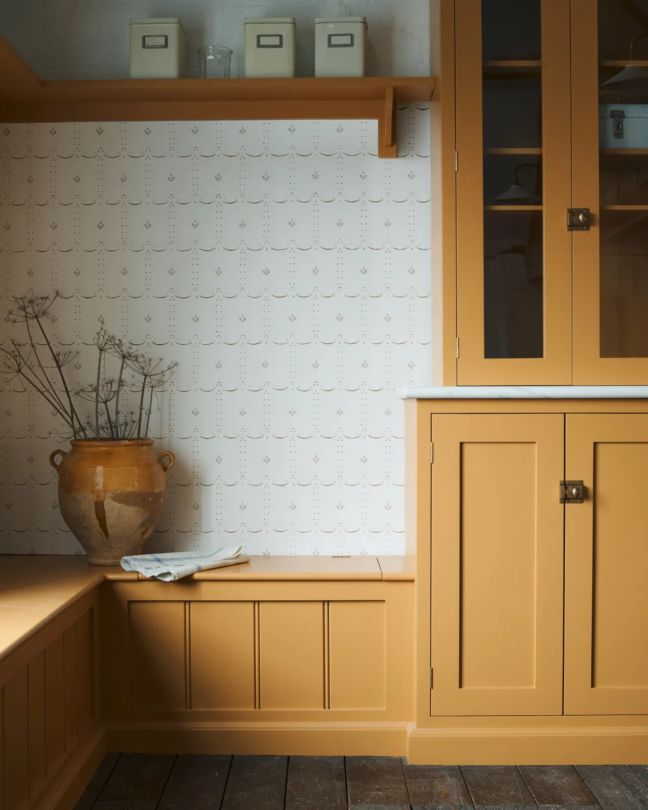 An off-white wallpaper with a delicate hand-painted pattern in a sepia colour, with surrounding deVOL's cupboards in mustard yellow colour.