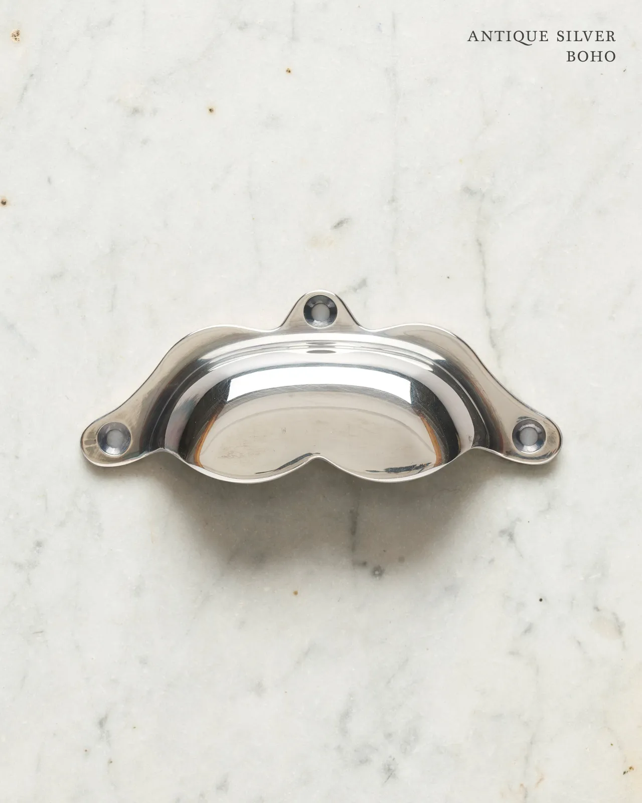A bohemian-style cup handle for a kitchen cupboard or drawer with a tarnished silver finish.