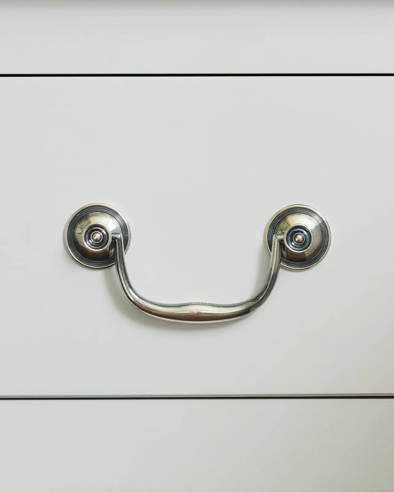 A front-on view of an elegant Georgian-style silver swing handle for kitchen cupboard drawers.