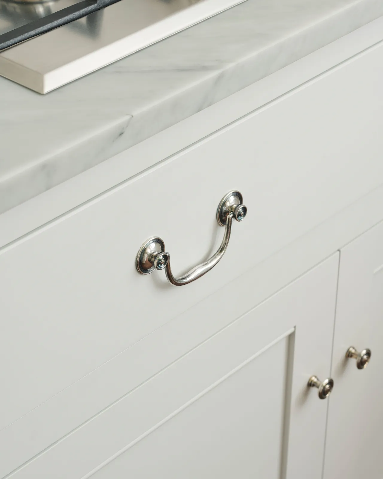 An angled view of an elegant Georgian-style silver swing handle fitted to a white painted kitchen drawer.