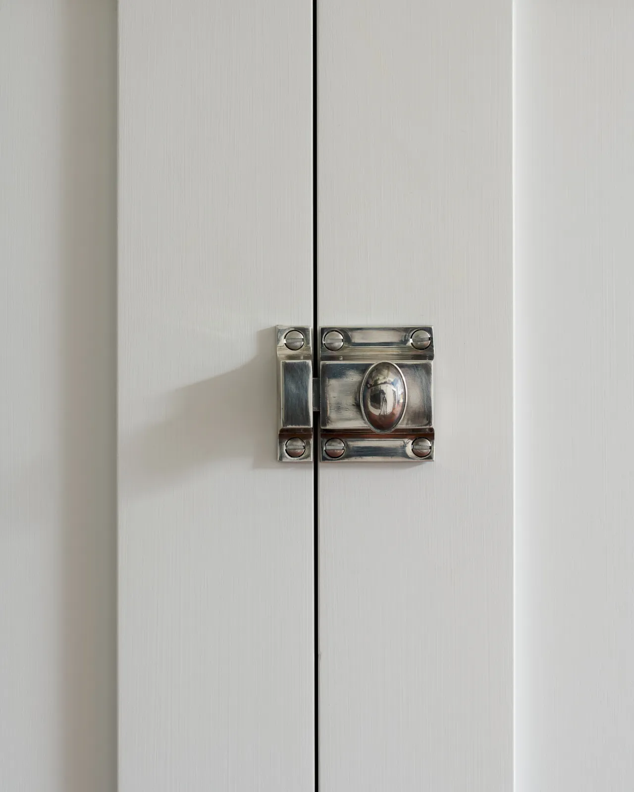 A straight-on view of a classic cupboard catch in a tarnished silver finish, fitted to a glazed white cupboard.