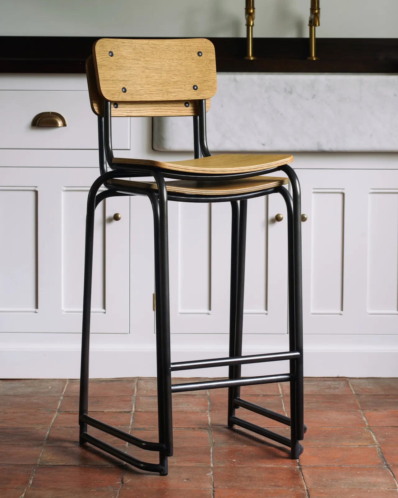Two mid-century-style industrial bar stools with a black tubular metal frame and shaped oak veneer plywood seat and backrest interlocked and stacked seamlessly on top of one another.