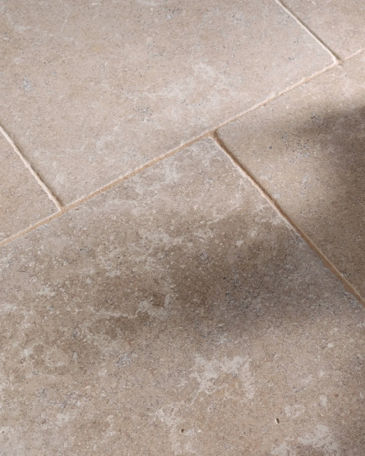 a close up image of the dijon tumbled limestone, looking soft and warm cream, with shadow casting on the tiles.