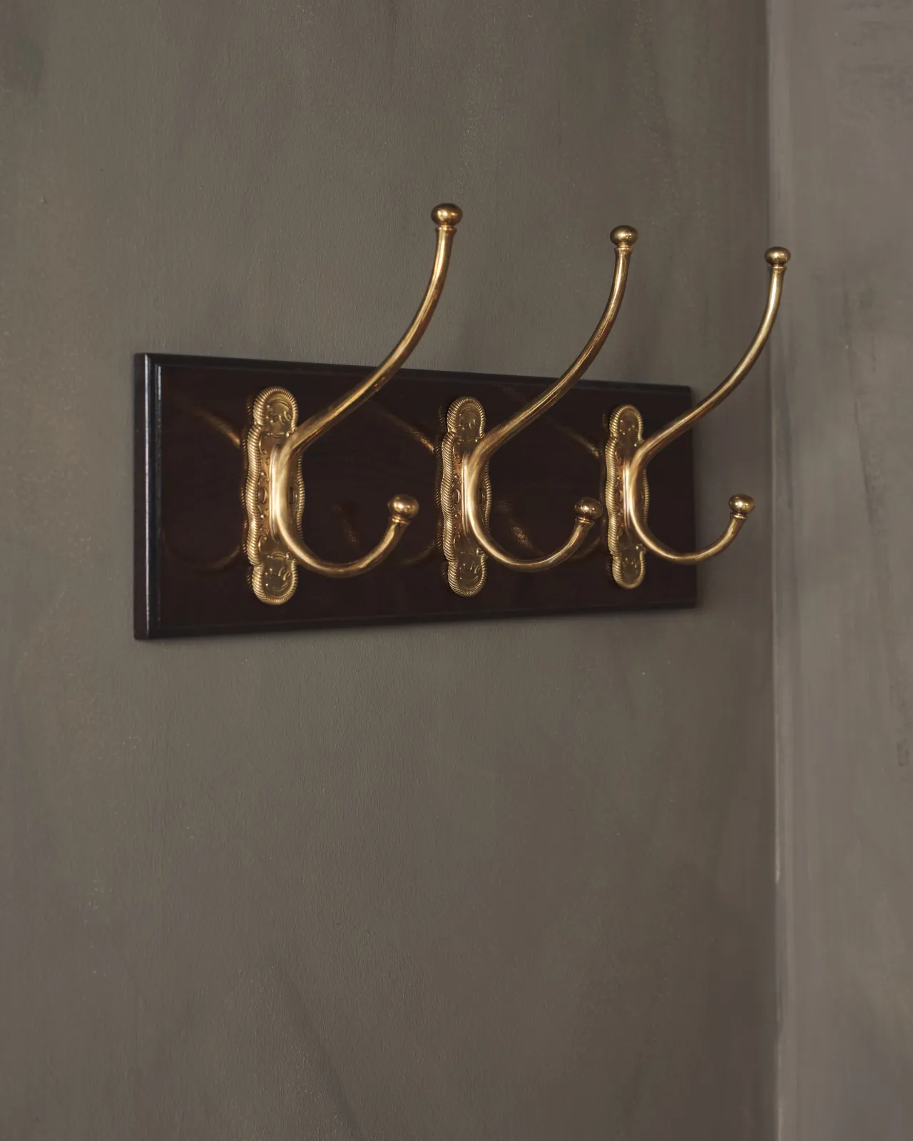 A close-up oblique view of a Mahogany Finish Hook Rack with three brass Grand Parisian Café Hooks.