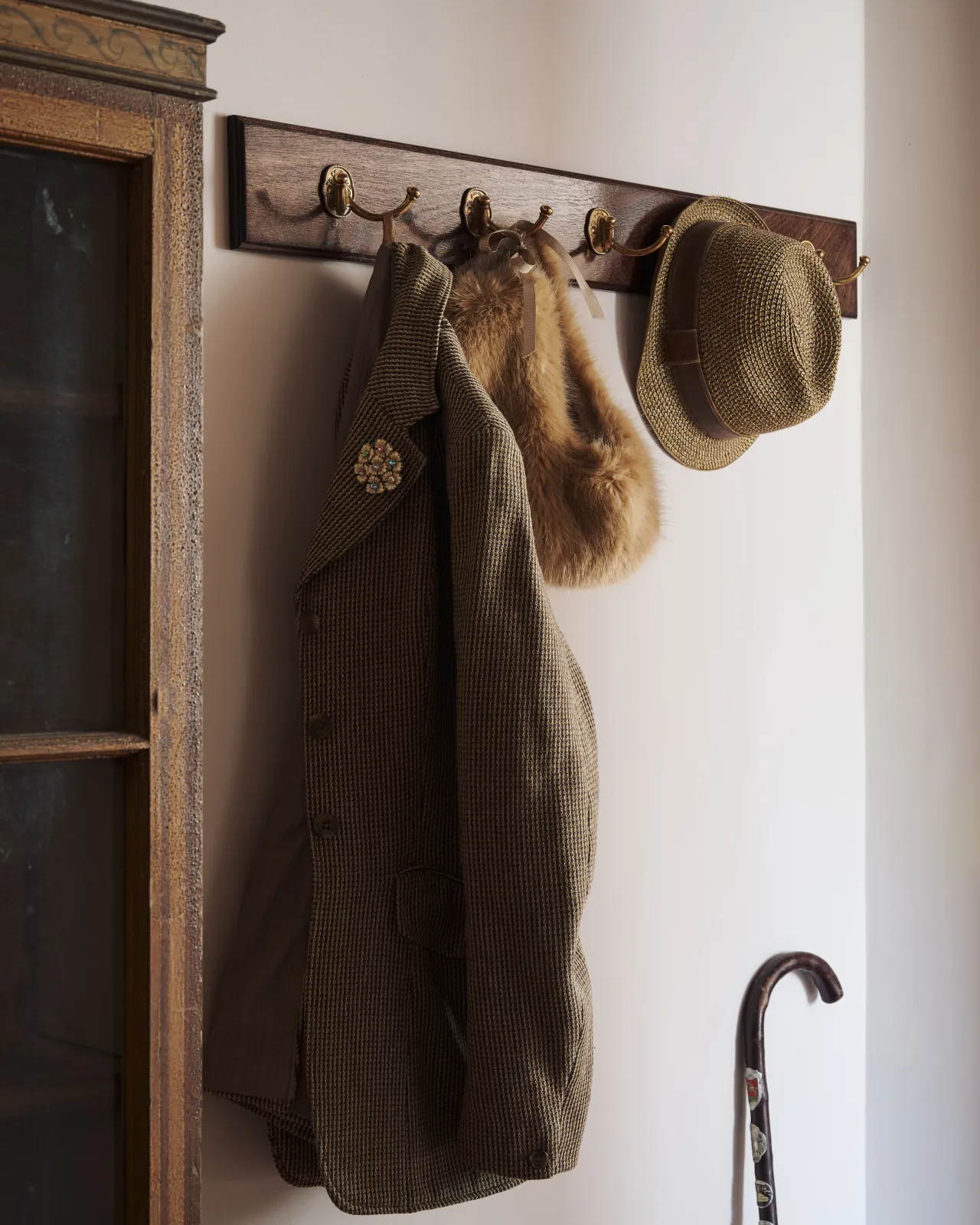 Five Twin Parisian Café Hooks on a Mahogany Finish backboard with a tweed jacket and hat hanging beside an antique dresser.