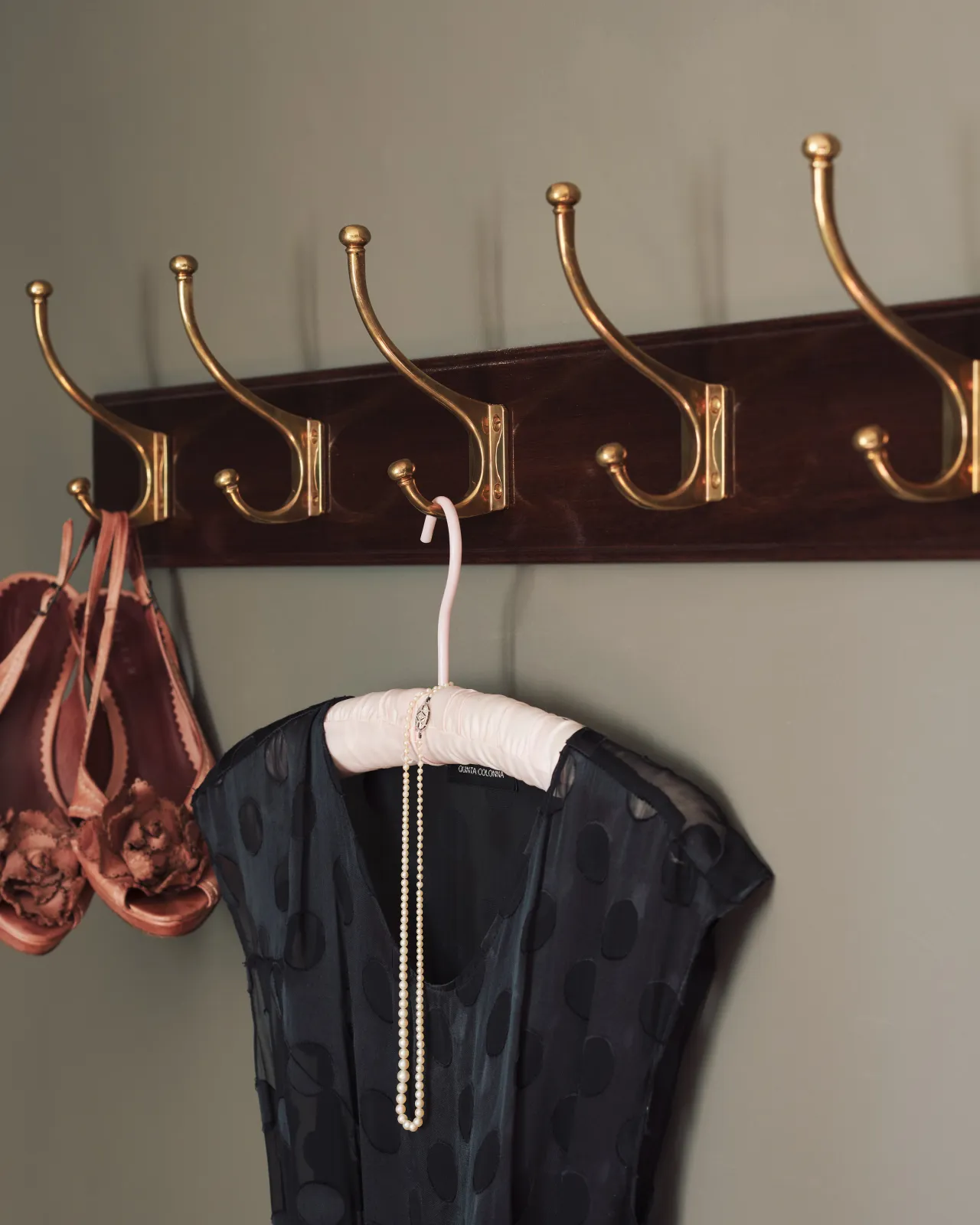 A close-up oblique view of a black lace dress and dusky pink shoes hanging from a Mahogany Finish Hook Rack with Edwardian brass hooks.